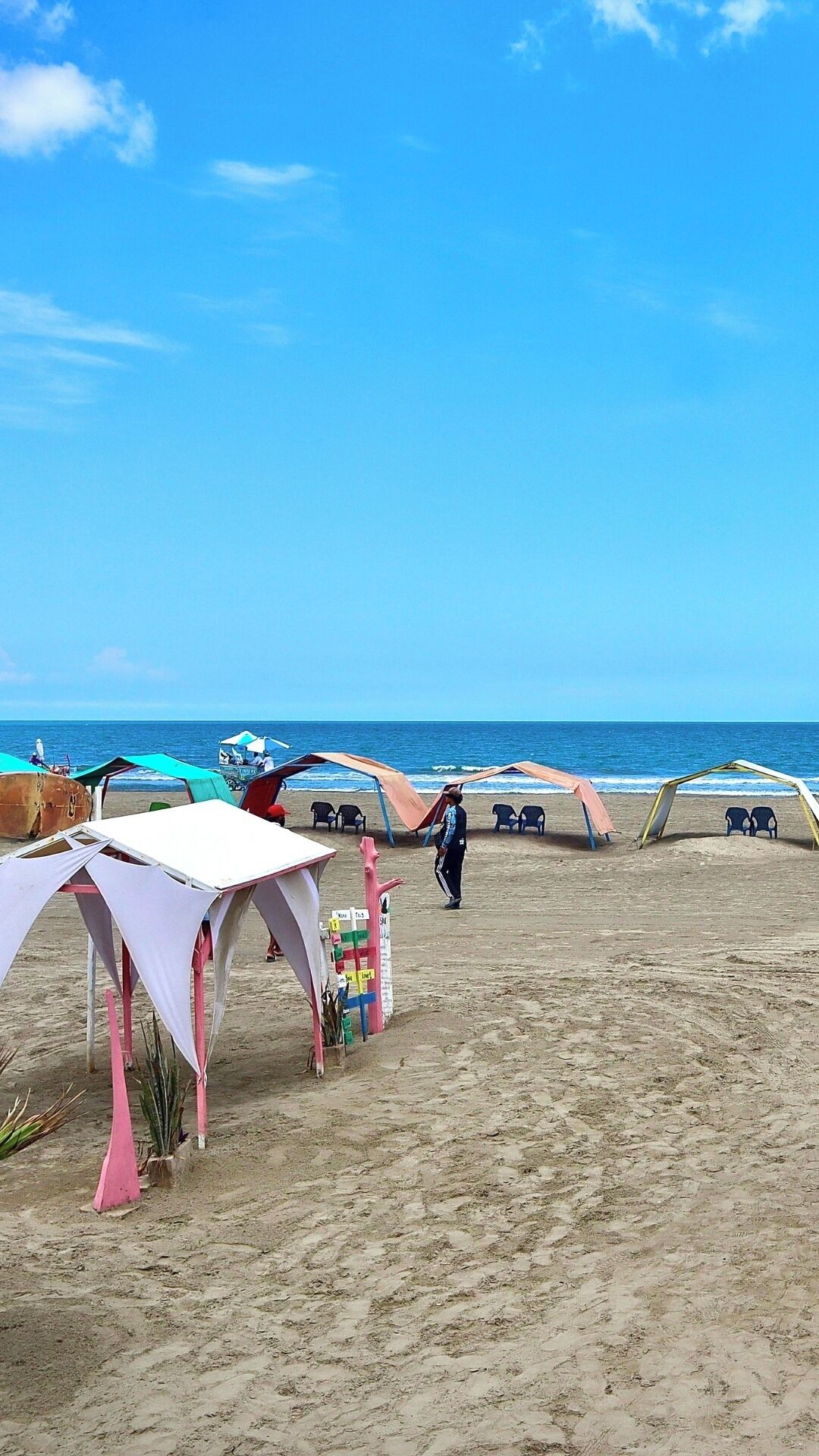 A beach with tents and chairs, a person walking, and a clear blue sky.