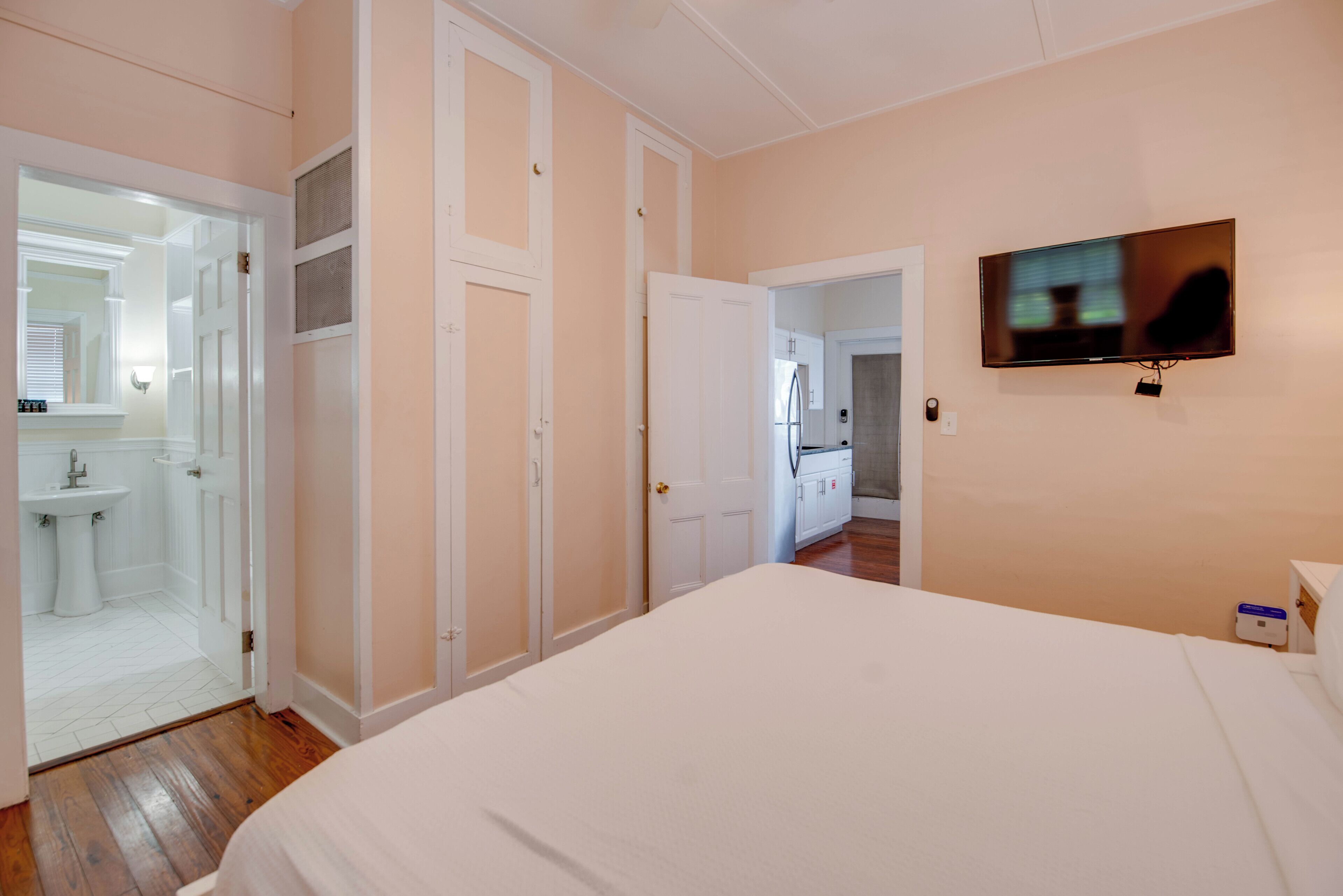 A bedroom with a bed, a TV, a bathroom with a sink, and a kitchen area.