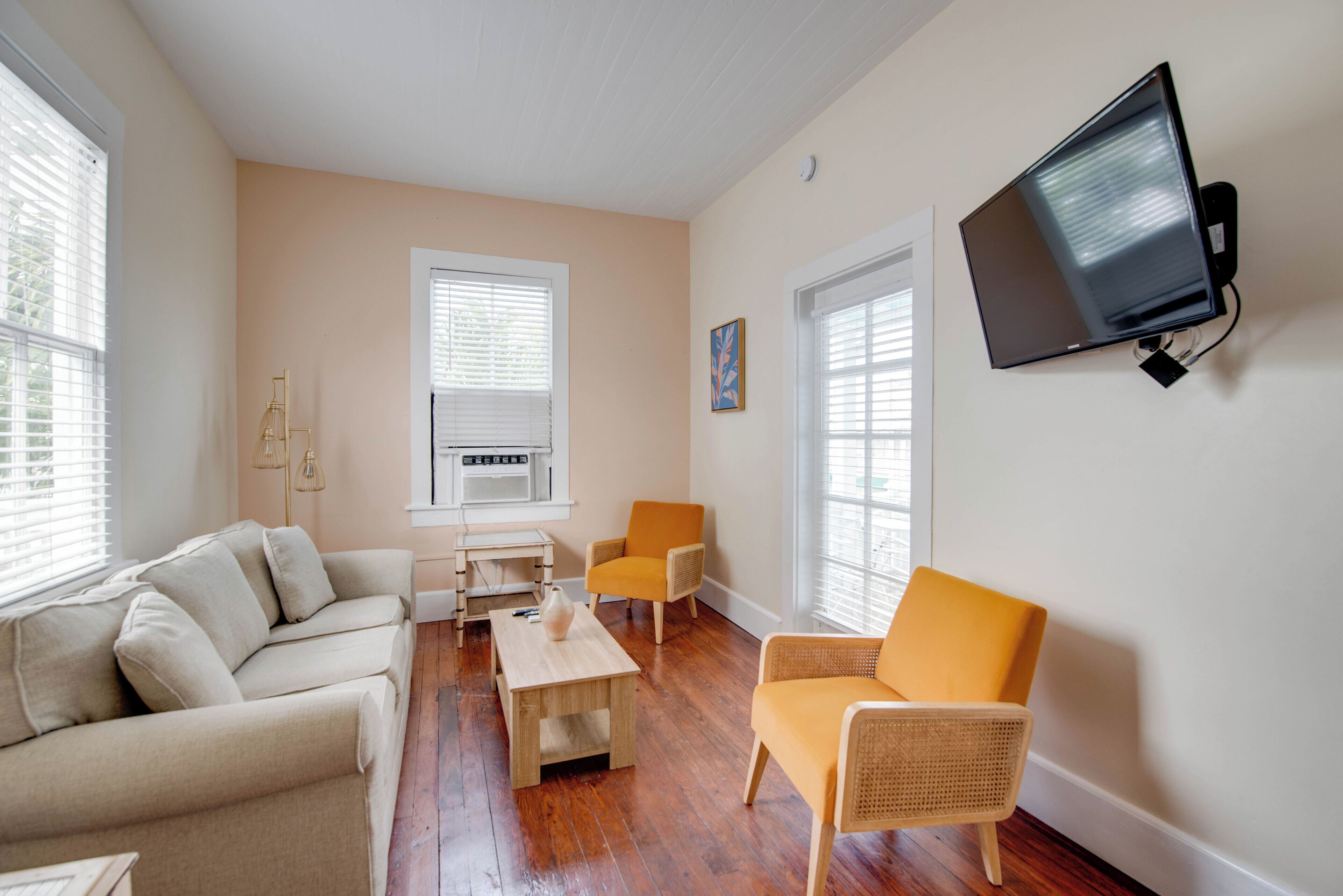 A living room with a sofa, two armchairs, a coffee table, and a flat-screen TV mounted on the wall.