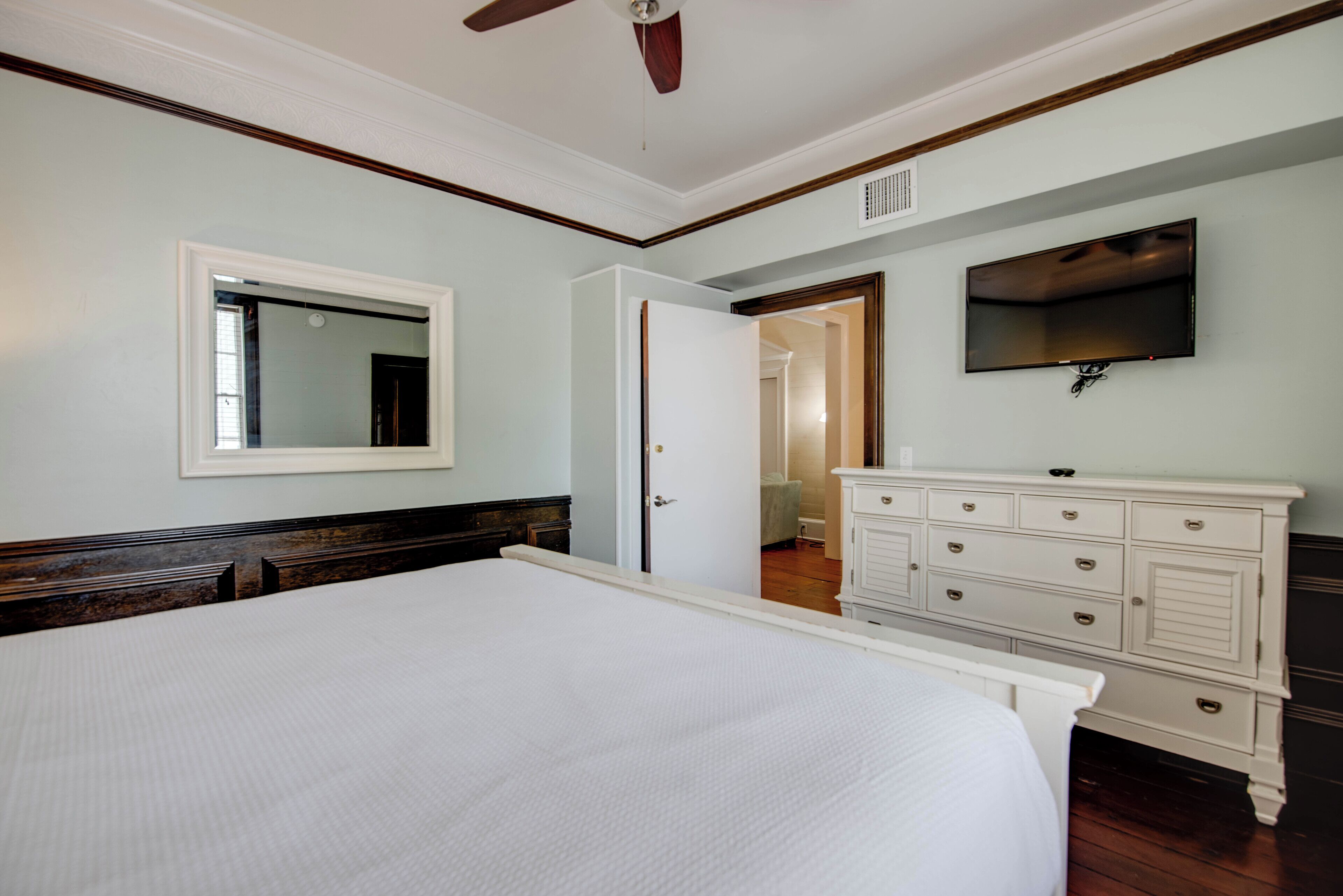 Een slaapkamer met een groot bed, een dressoir, een spiegel en een televisie aan de muur.