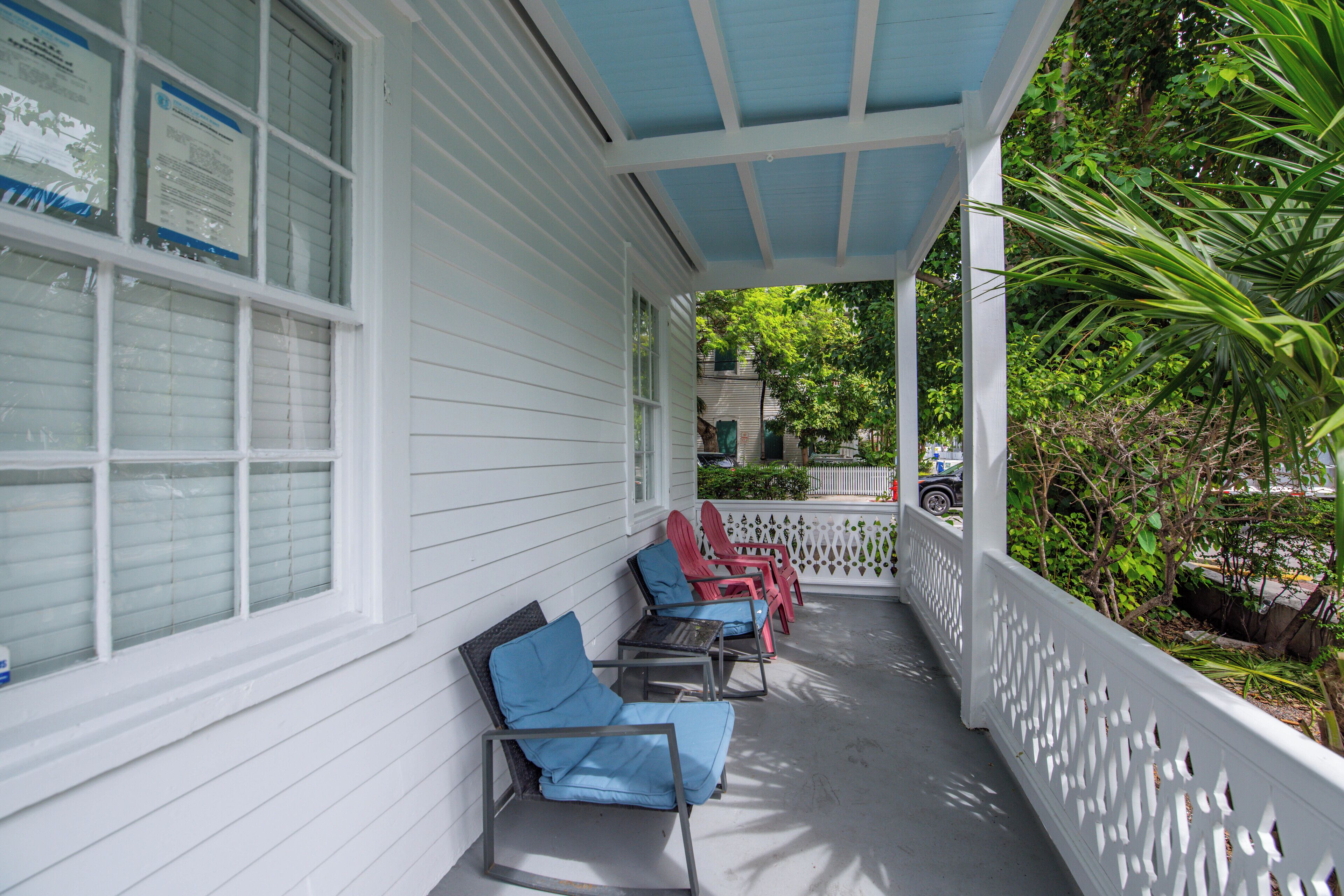 A covered porch with white railings and blue cushions on chairs.