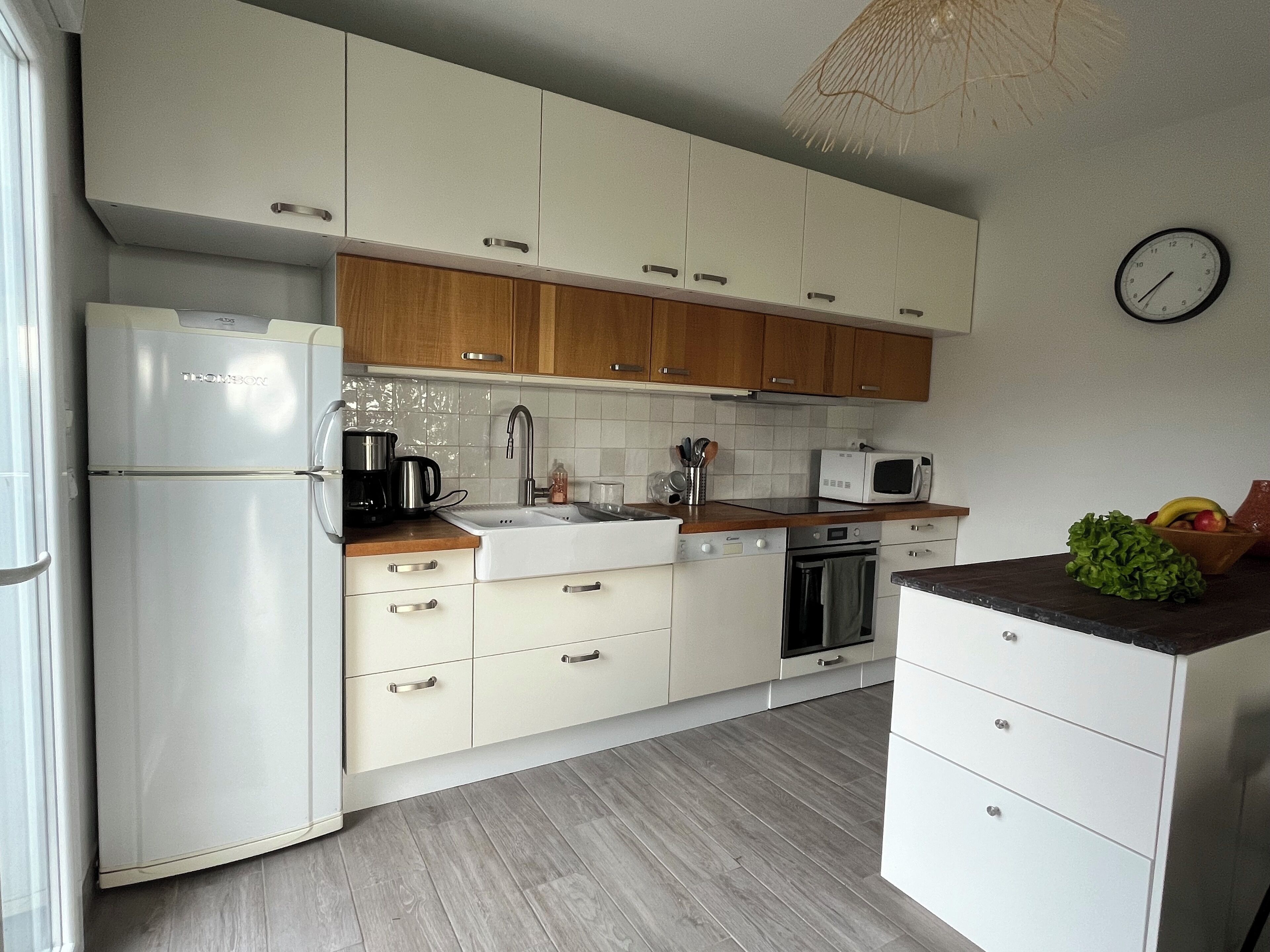 Une cuisine moderne avec des meubles blancs et en bois, un réfrigérateur, une machine à café, un four à micro-ondes et un évier.