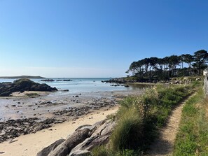 A coastal landscape with a sandy beach, rocky outcrops, and a path leading to a building surrounded by trees. - House on the seafront (160m) and GR34, peaceful setting for weekends and vacations. (Guissény)