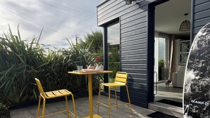 Eine moderne Außenpatio mit einem Holztisch und zwei gelben Stühlen, einem großen Fenster und Blick ins Hausinnere.