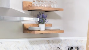 A kitchen with wooden shelves holding wine glasses and plates, a modern stove, and a herringbone-patterned backsplash.