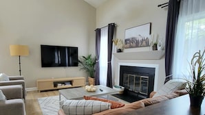 A modern living room with a fireplace, a flat-screen TV, and a ceiling fan.