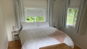 A bedroom with a large bed, a wooden bench, a nightstand with a lamp, and a window with curtains. - Silva Bay View, a boutique, private BnB with a great view (Gabriola)