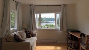 A cozy room with a sofa, a table, and a view of a lake and forest. - Silva Bay View, a boutique, private BnB with a great view (Gabriola)