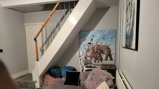 A living room with a staircase, a painting of elephants and butterflies, and a radiator. - Apartment - Sleeps 5 - Great Location - Parking (Stoke-on-Trent)