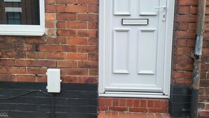 A white door with a black and red brick wall, a small window, and a white electrical box. - Apartment - Sleeps 5 - Great Location - Parking (Stoke-on-Trent)