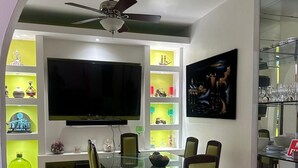 Un comedor moderno con una mesa de vidrio, sillas verdes, un televisor de pantalla plana grande y estantes decorativos.