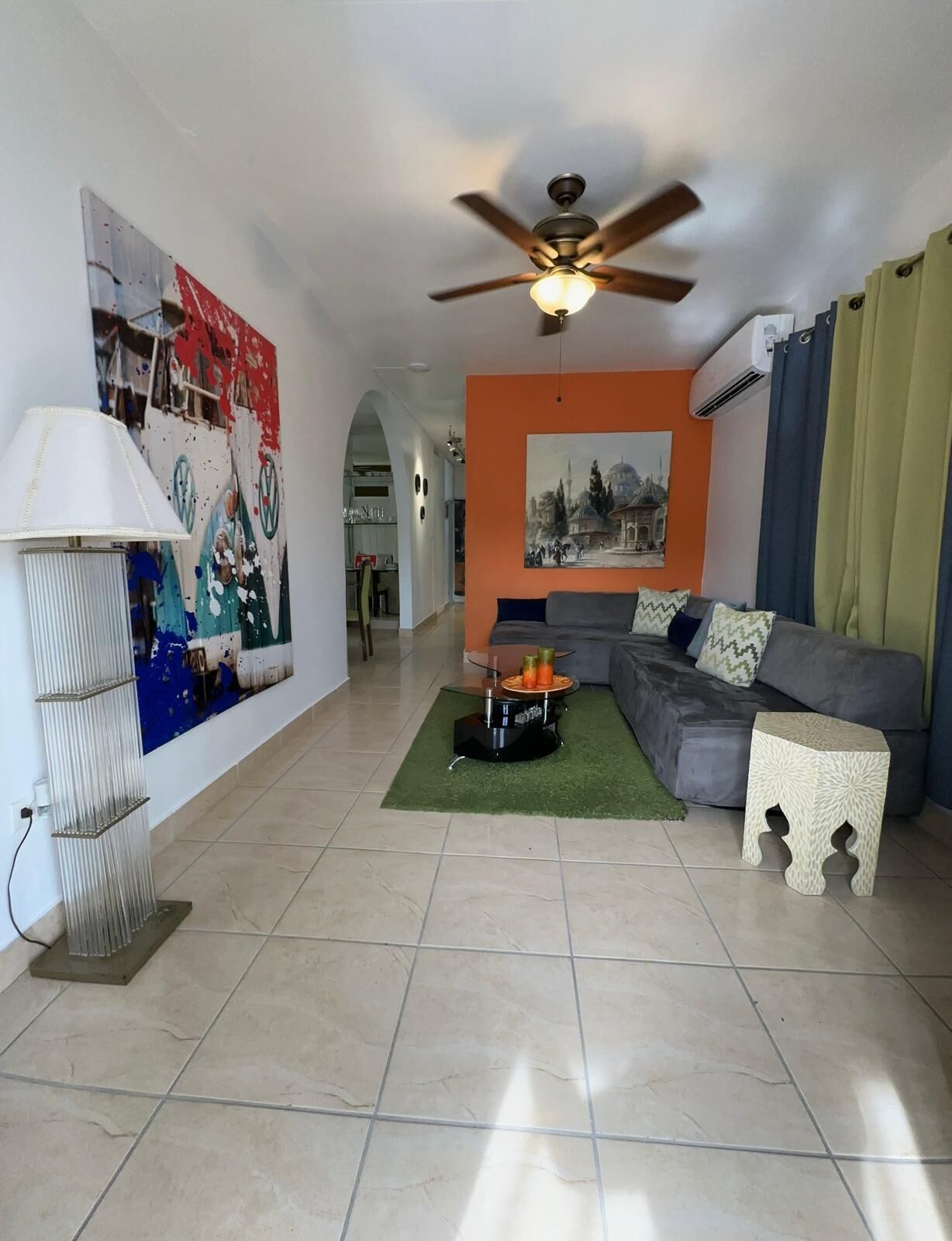 A living room with a sofa, a coffee table, a lamp, a ceiling fan, and a painting on the wall.