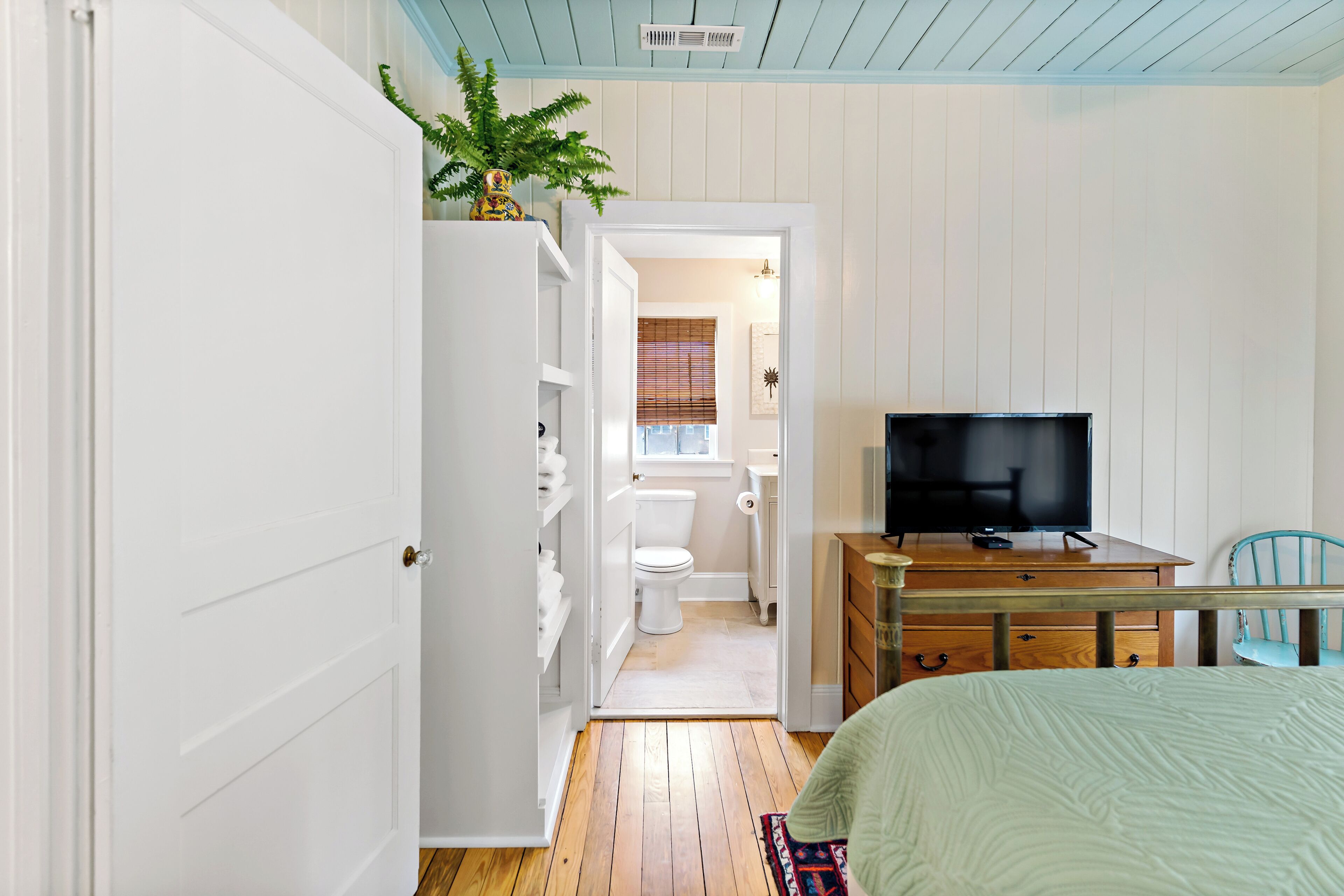Una camera da letto con un letto, una televisione, una scrivania e una sedia. Si intravede un bagno attraverso una porta aperta.