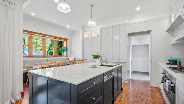 A modern kitchen with a large island, white cabinetry, and a herringbone wood floor. - Spacious heritage home (Moonee Ponds)