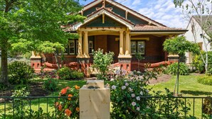 A two-story house with a front porch, brick exterior, and a well-maintained garden with various plants and flowers. - Spacious heritage home (Moonee Ponds)