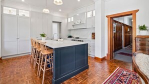 A modern kitchen with white cabinetry, a central island with bar stools, and a herringbone wood floor. - Spacious heritage home (Moonee Ponds)