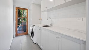 A compact kitchen with white cabinets, a built-in sink, and a washing machine. - Spacious heritage home (Moonee Ponds)