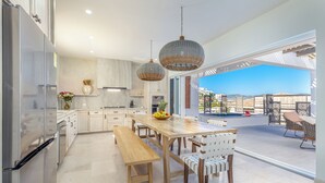 Una cocina moderna con una mesa de comedor de madera, sillas blancas y un amplio ventanal con vistas a una piscina.