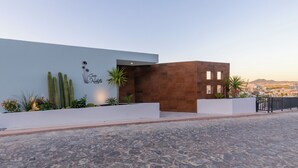 Un edificio moderno con fachada blanca y sección marrón, que presenta un jardín de cactus y vistas a la ciudad.