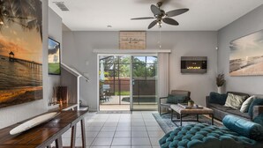Ein modernes Wohnzimmer mit einer Couch, einem Couchtisch und einem Fernseher. An der Wand hängt ein Gemälde, und es gibt einen Deckenventilator.