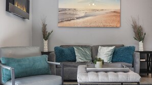 Ein Wohnzimmer mit grauem Sofa, türkisfarbenen Kissen, einem grauen Sessel und einem Couchtisch mit einer Pflanze.