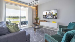 A modern living room with a sofa, armchairs, a coffee table, and a TV on the wall.