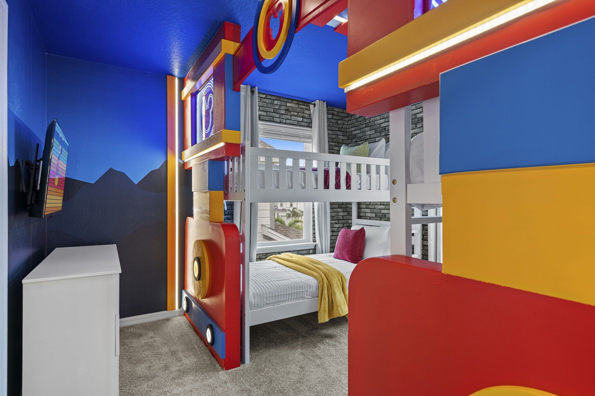 Habitación infantil con literas, un aparador blanco y decoraciones de pared coloridas.