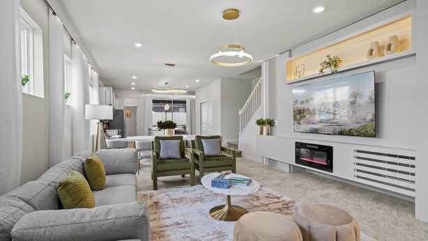A modern living room with a grey sofa, green armchairs, a round coffee table, and a flat-screen TV mounted on the wall.