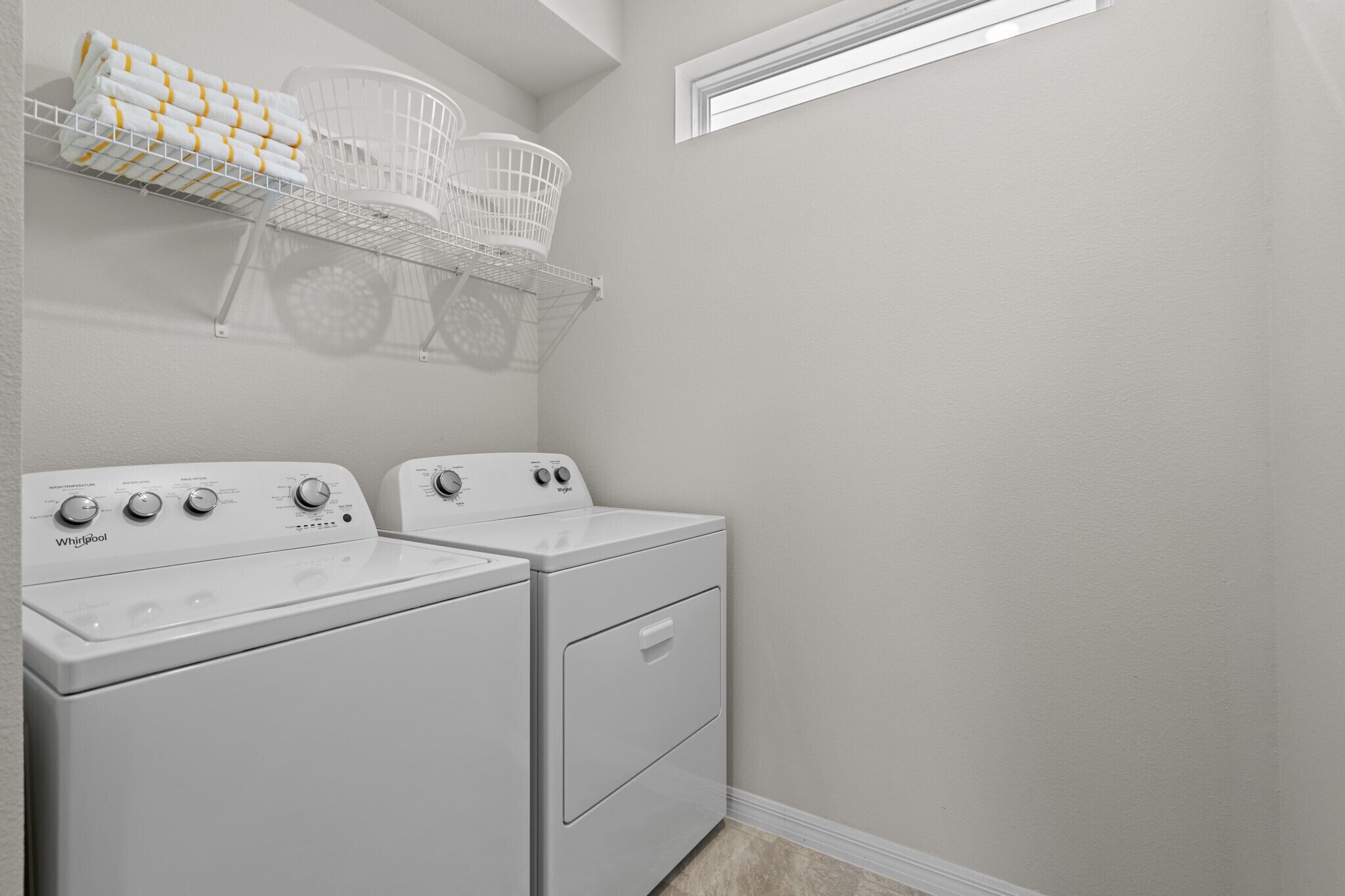 A laundry room with two white Whirlpool washers and dryers, a metal laundry basket, and a white towel rack.