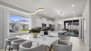 A modern kitchen with white cabinets, a central island, and a dining area with grey chairs.