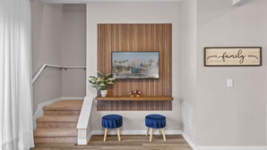 Eine Treppe mit einer Wand aus Holzpaneelen, einem gerahmten Bild einer Weltkugel, zwei blauen Hocker und einem kleinen Regal mit einer Pflanze und Figuren.