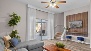Ein modernes Wohnzimmer mit einem grauen Sofa, einem Holztisch und einem Deckenventilator.