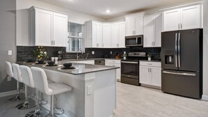 A modern kitchen with white cabinets, stainless steel appliances, and a central island with bar stools. - Last Minute Disney! Private Pool, Game Room & Themed Bedrooms. Book Now! #121915 (Orlando)