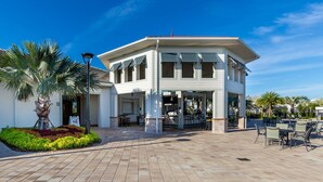 A white building with a covered patio area, outdoor seating, and a landscaped garden with palm trees. - Last Minute Disney! Private Pool, Game Room & Themed Bedrooms. Book Now! #121915 (Orlando)