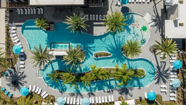 Luchtbeeld van een resort met een groot, onregelmatig zwembad, omringd door palmbomen en ligbedden.