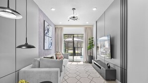 Een moderne woonkamer met een grijze bank, een zwart tv-meubel en een vloerkleed met een geometrisch patroon.