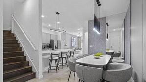 Een moderne keuken met een centraal eiland, barstoelen, hanglampen en een trap naar een ander niveau.