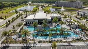 Een resort met een centraal gelegen zwembad, palmbomen en een groot gebouw op de achtergrond.