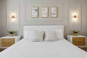 A bedroom with a large bed, two bedside tables with plants, and wall-mounted light fixtures.