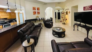 A modern living room with a sofa, armchairs, a coffee table, and a television. There is a kitchen area with cabinets and a microwave. A ceiling fan and pendant lights are visible. - Casa Colibrí
UltraWIFI, HOTTUB, POOL, PLAYPEN, 2KING BEDS, MULTI FAMILY FRIENDLY (Harlingen)