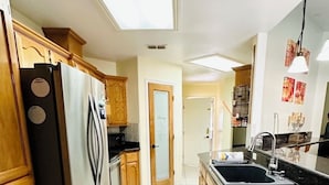 A kitchen with wooden cabinets, a stainless steel refrigerator, a black countertop, and a tiled floor. - Casa Colibrí
UltraWIFI, HOTTUB, POOL, PLAYPEN, 2KING BEDS, MULTI FAMILY FRIENDLY (Harlingen)