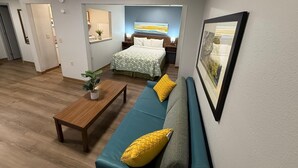 Ett kompakt bostadsutrymme med en säng, en soffa, ett litet bord och en tavla som hänger på väggen.