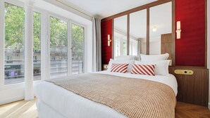 Ein Hotelzimmer mit einem großen Bett, Blick auf die Stadt durch raumhohe Fenster und einer roten Akzentwand.