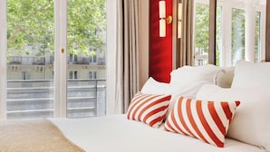 Ein Hotelzimmer mit großem Fenster, einem Bett mit weißer Bettwäsche und gestreifteren Kissen.