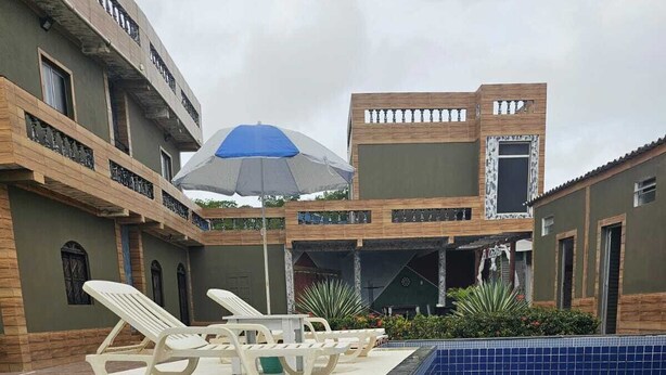 Une piscine dotée de chaises longues et d’une terrasse carrelée, entourée d’immeubles avec balcons et d’un espace salon couvert.