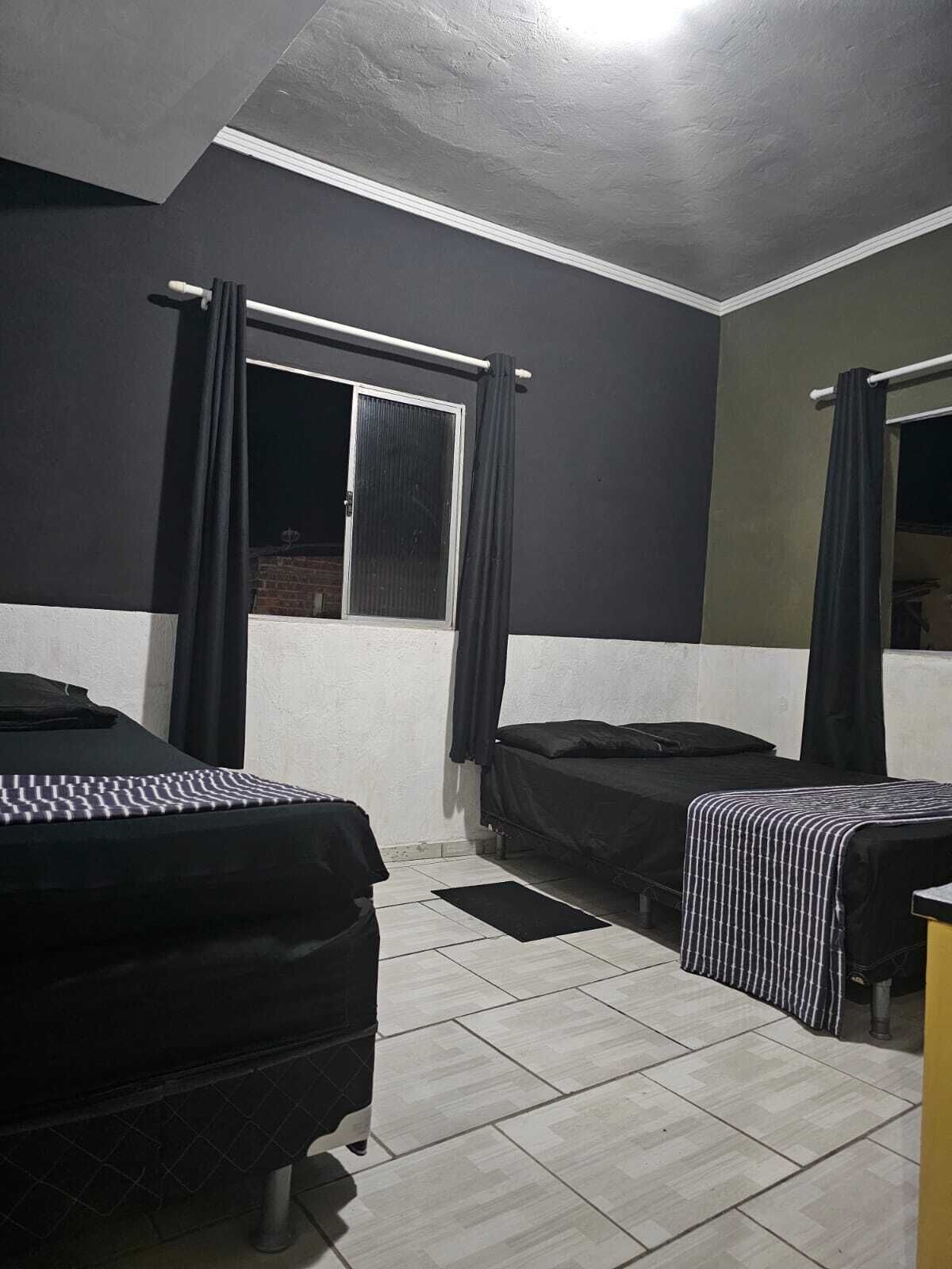 Ein Zimmer mit zwei Betten, einem fensterbelaubten Fenster und einem Fliesenboden.