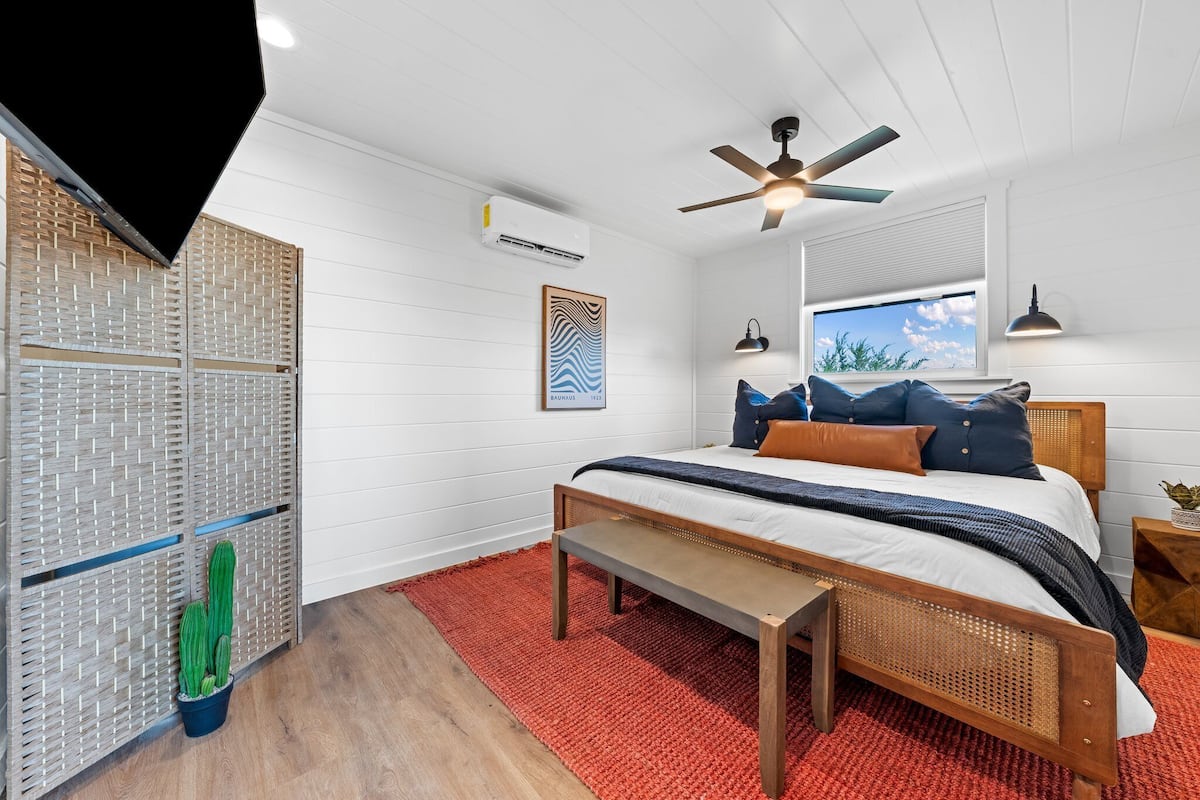 Een slaapkamer met een bed, een plafondventilator, een raam met uitzicht en een cactus.