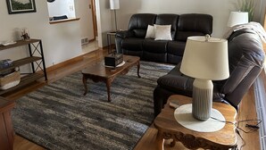 Een woonkamer met een zwarte leren bank, een houten salontafel, een lamp en een vloerkleed.
