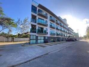 A multi-story residential building with balconies, a paved street, and parked cars.