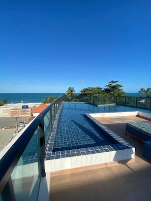 A rooftop pool with a clear view of the ocean, surrounded by greenery and a modern architectural design.